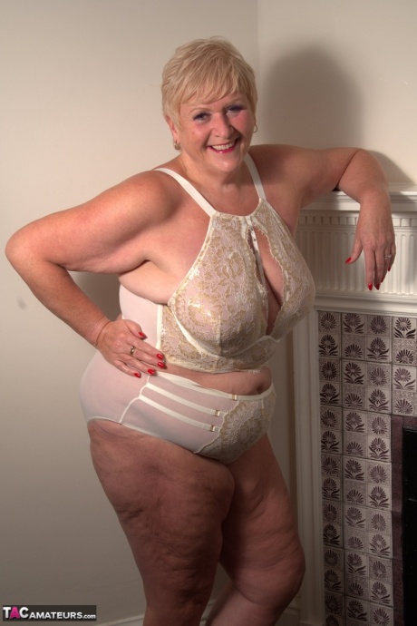 Зрелая толстушка с короткими светлыми волосами полностью раздевается на своей кровати 6