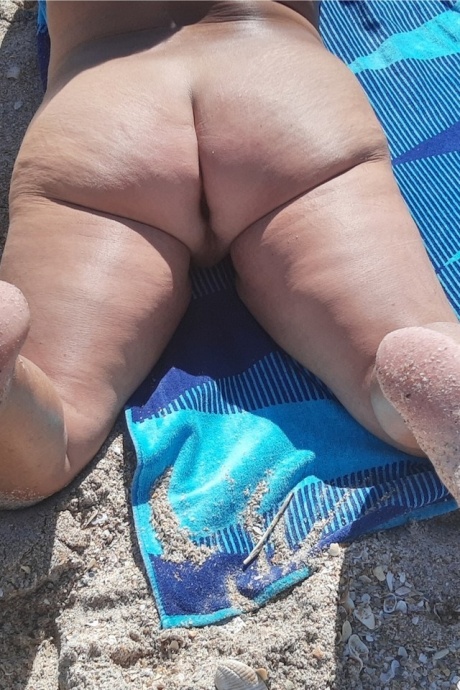 Пожилая любительница Дебби Делишес загорает в тени на нудистском пляже 5